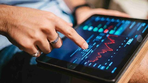 A fingertip touches the screen of a table showcasing a trading chart